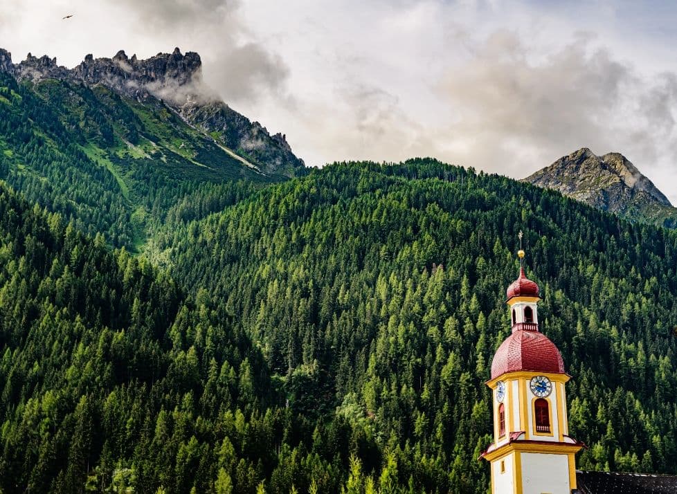 Kirchturm zwischen bewaldeten Hängen im Stubaital